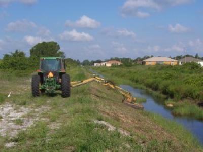 Tractor with slope mower arm attachment mowing grass on a canal bank
